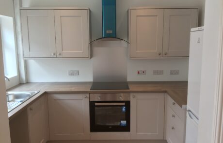 Contemporary kitchen designed and installed by Hummingbird Bathrooms and Kitchens, featuring light cupboards, wooden worktops, built-in oven, electric hob, stylish blue extractor hood, left-side sink, and a white fridge on the right. Brightly lit space showcasing expertly crafted kitchen refurbishment in the UK. Contemporary kitchen designed and installed by Hummingbird Bathrooms and Kitchens, featuring light cupboards, wooden worktops, built-in oven, electric hob, stylish blue extractor hood, left-side sink, and a white fridge on the right. Brightly lit space showcasing expertly crafted kitchen refurbishment in the UK.
