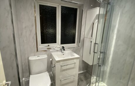 Modern bathroom design by Hummingbird Bathrooms and Kitchens, featuring a curved glass shower enclosure, white toilet, sink vanity with drawers, large window for natural light, and grey patterned walls and flooring. Expertly illuminated by bright ceiling lights. Specialists in bathroom installation, kitchen refurbishments, construction services and interior design across the UK. Modern bathroom design by Hummingbird Bathrooms and Kitchens, featuring a curved glass shower enclosure, white toilet, sink vanity with drawers, large window for natural light, and grey patterned walls and flooring. Expertly illuminated by bright ceiling lights. Specialists in bathroom installation, kitchen refurbishments, construction services and interior design across the UK.
