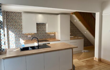 Contemporary kitchen design by Hummingbird Bathrooms and Kitchens, featuring sleek white cabinetry, wooden worktops, stylish patterned tiled splashback, and a modern black sink. Wooden staircase with bannisters visible in the background and natural sunlight highlighting this bespoke UK kitchen renovation. Contemporary kitchen design by Hummingbird Bathrooms and Kitchens, featuring sleek white cabinetry, wooden worktops, stylish patterned tiled splashback, and a modern black sink. Wooden staircase with bannisters visible in the background and natural sunlight highlighting this bespoke UK kitchen renovation.